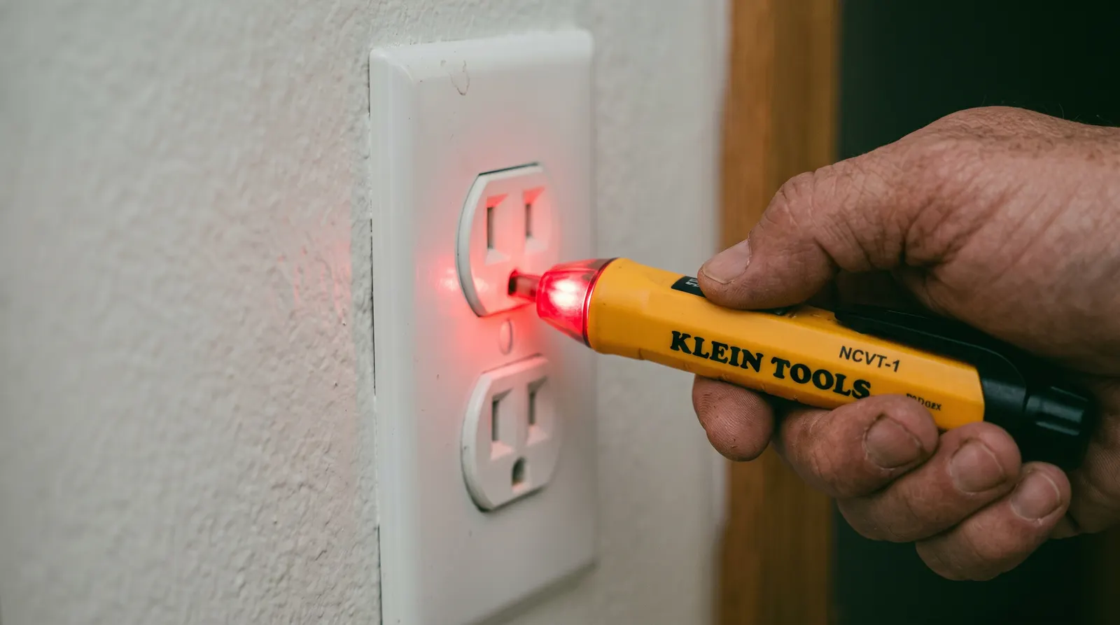 Non-contact voltage tester held against a receptacle showing an active indication
